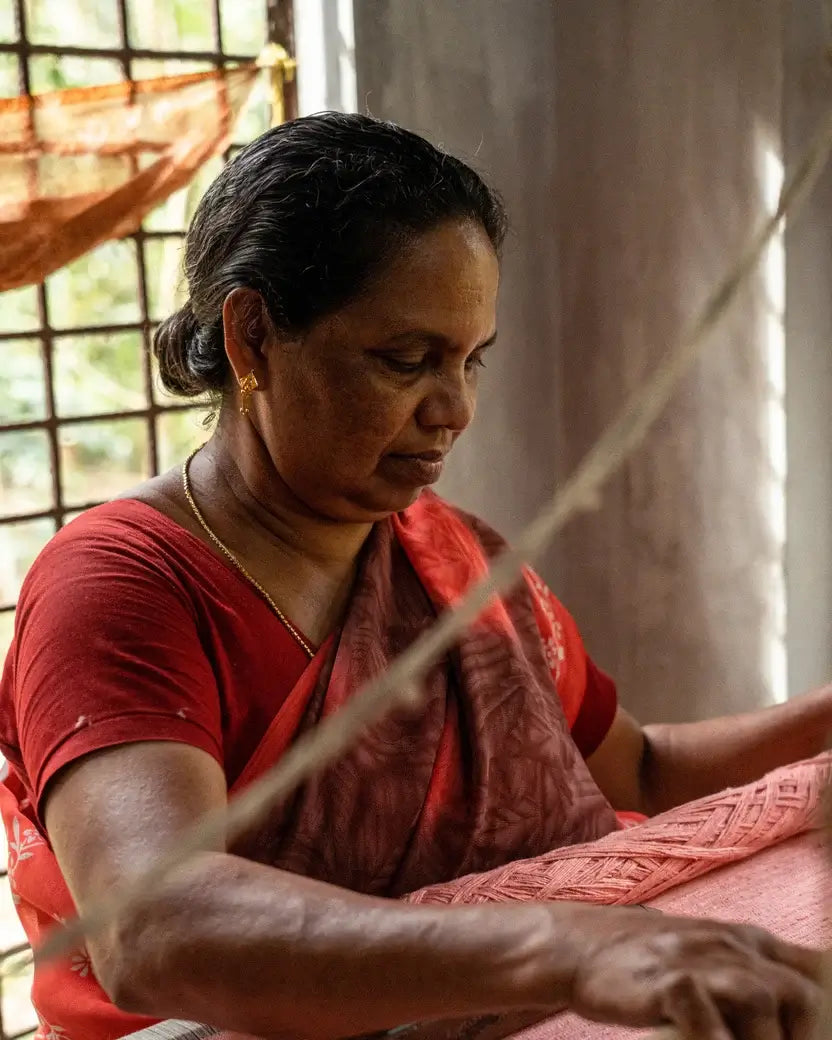 Woman in a red sari working on a piece of fabric. 
